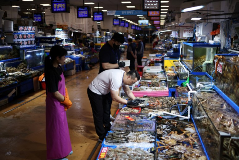 An official checking radiation levels of imported scallops in a Seoul market. There are stalls piled with seafood along either side. 