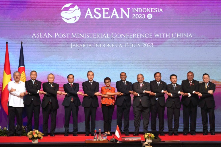 Asean foreign ministers pose for a group photo after their meeting in Jakarta. They are have their arms crossed in front to hold each others hands. Indonesia's foreign minister Retno Marsudi is in the middle., and the only woman.
