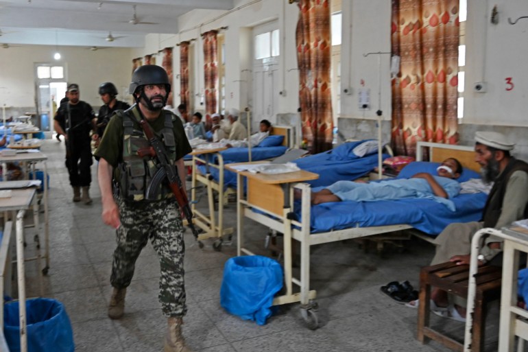 Security personnel walk past bomb blast victims at a hospital in Bajaur district of Khyber-Pakhtunkhwa province on July 31, 2023. - At least 44 people were killed and more than 100 others wounded on July 30 by a suicide bombing at a political gathering of a leading Islamic party in northwest Pakistan, officials said. (Photo by Abdul MAJEED / AFP)