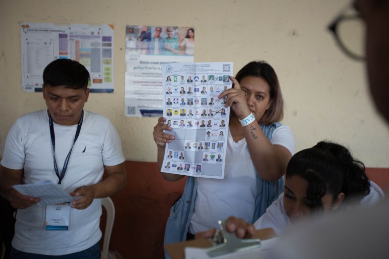 A woman holds up a ballot, where a pair of candidates are crossed out with an X.