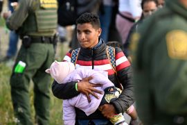 An asylum seeker carries his baby past US Border Patrol agents as they wait between the double fence along the US-Mexico border near Tijuana, Mexico, May 8, 2023