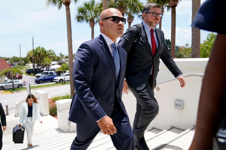 A bald man in a suit walks up the steps to a Miami courthouse.