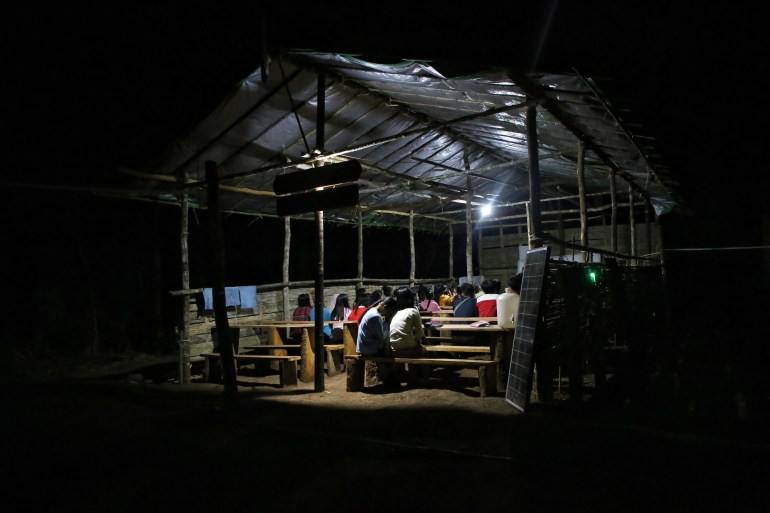 An evening class for students in Myanmar. They are in a dimly lit shelter and it's pitch black all around.