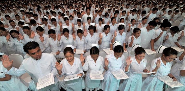 Women in rows wearing white nurses' uniforms and hats all have their right hand up, with their left holding a document they are reading from.