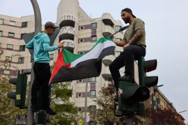 Two people hold a Palestine flag on top of a traffic light