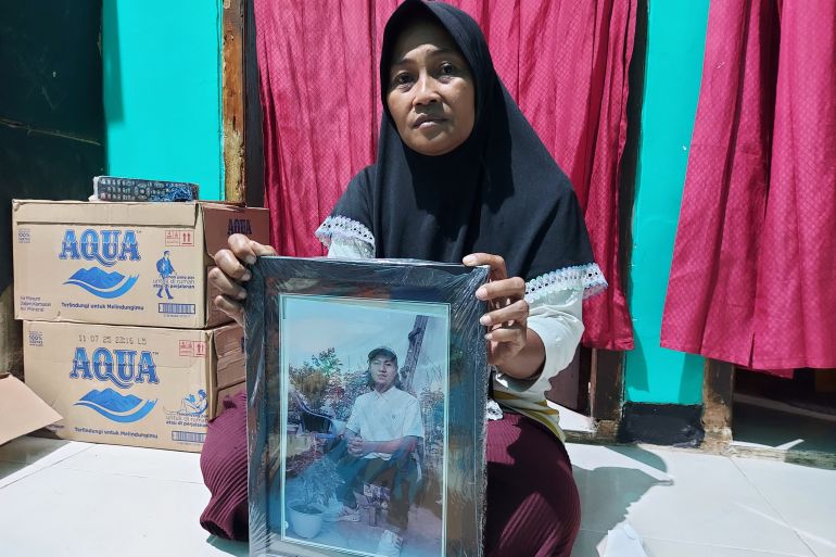 Rini Hanifa holds a picture of her son Agus. She is seated on the floor holding up the large framed photo