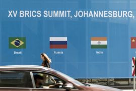 A woman walks past a poster for the 2023 BRICS Summit at the Sandton Convention Centre in Sandton, Johannesburg, on August 20, 2023. - The BRICS countries, an acronym of the five members Brazil, Russia, India, China and South Africa, meet for three days for a summit in Johannesburg starting August 22, 2023. (Photo by MARCO LONGARI / AFP)