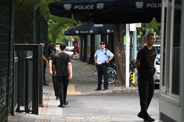 Plain clothes police and security officials outside the Japanese embassy in Beijing. They are dressed in black. There are black canopies with the word 'police'.