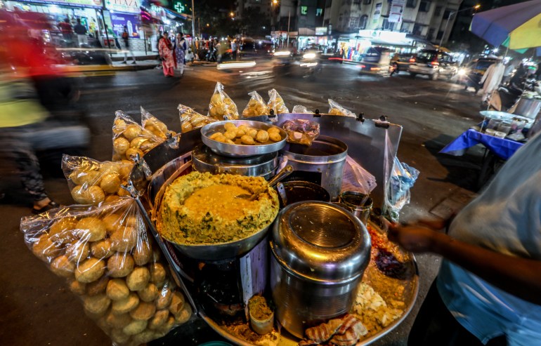 An Indian street food vendor sells the common street snack Panipuri, fried puris with an assortment of fillings, as commuters walk past in Mira Road, on the outskirts of Mumbai