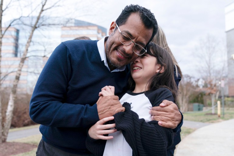 Former Nicaragua presidential candidate Felix Maradiaga hugs his young daughter Alejandra, outside on a sidewalk in the Washington, DC, area. She hides her face in his neck as he smiles and wraps his arms around her.