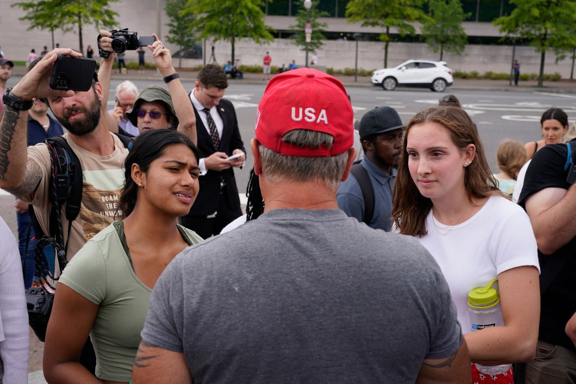 A supporter of Former President Donald Trump, center with red cap, talks with protesters
