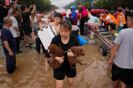 A woman carries her pet dogs as residents are evacuated on rubber boats through floodwaters in Zhuozhou in northern China's Hebei province, south of Beijing