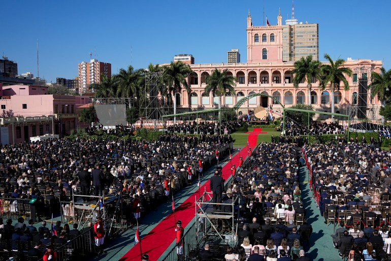 A red carpet stretches from the presidential palace through a crowd of onlookers.
