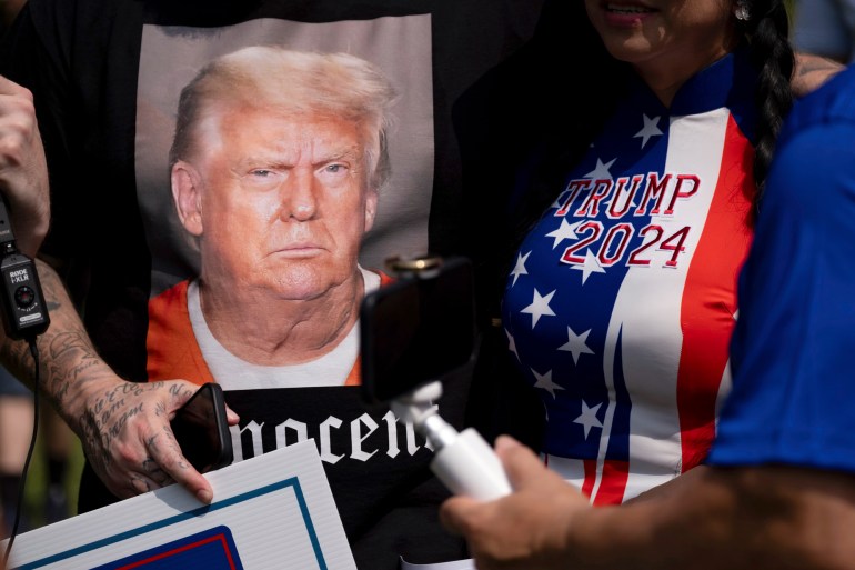 A close-up of Trump supporters wearing red-white-and-blue shirts and posters showing Trump in a prison jumpsuit.
