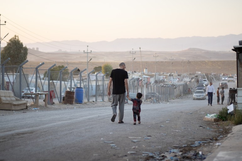 A man walking down the road in the camp holding the hand of a small child