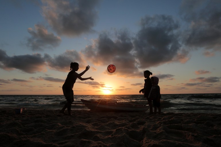 children playing ball on the beach against a setting sun