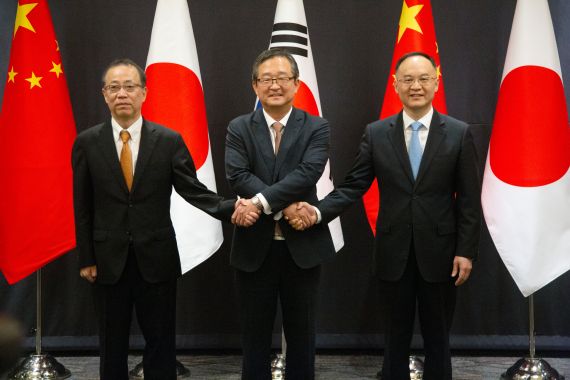 The three officials from Japan, South Korea and China shaking hands in front of their national flags