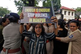 A demonstrator holds up a placard, as police officers detain others during a protest against the alleged sexual assault of two tribal women in the eastern state of Manipur, in Ahmedabad, India