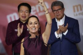 Former Mexico City Mayor Claudia Sheinbaum smiles and lifts her arm into the air as she celebrates being named presidential candidate. She is standing on stage.