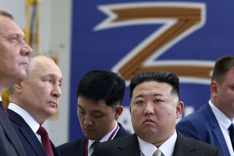 Kim Jong Un and Vladimir Putin at their meeting in Russia. They are surrounded by officials. There is a banner with the letter Z behind them.