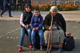 An elderly woman and children sit on bags of belongings as residents gather in central Stepanakert to leave Nagorno-Karabakh [David Ghahramanyan/Reuters]