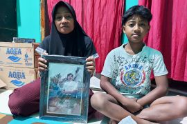 Rini Hanifa holds a photo of her son who died in the disaster while sitting next to his younger brother [Aisyah Llewellyn/Al Jazeera]