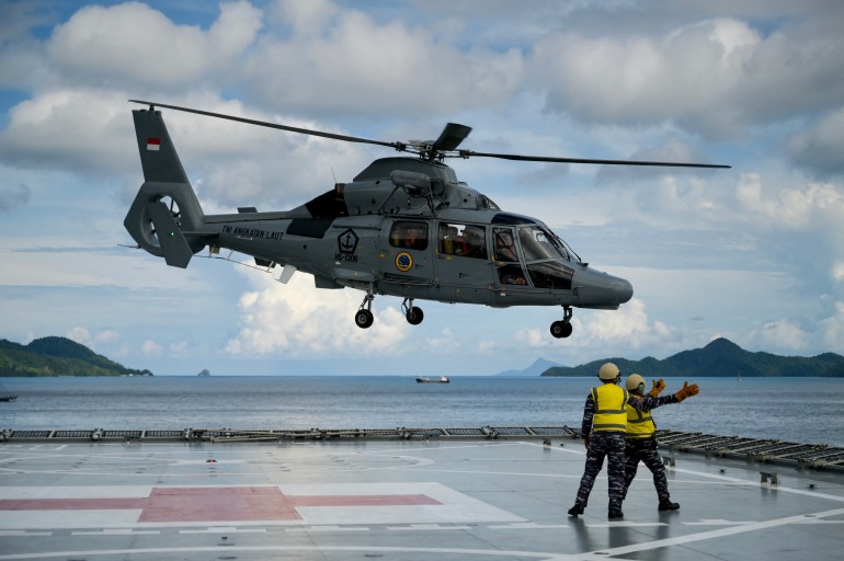 anther helicopter takes off from the deck of a ship. Two men are on deck