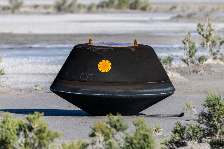 The capsule containing the asteroid samples in the desert. It is black and shaped a like a lozenge. 