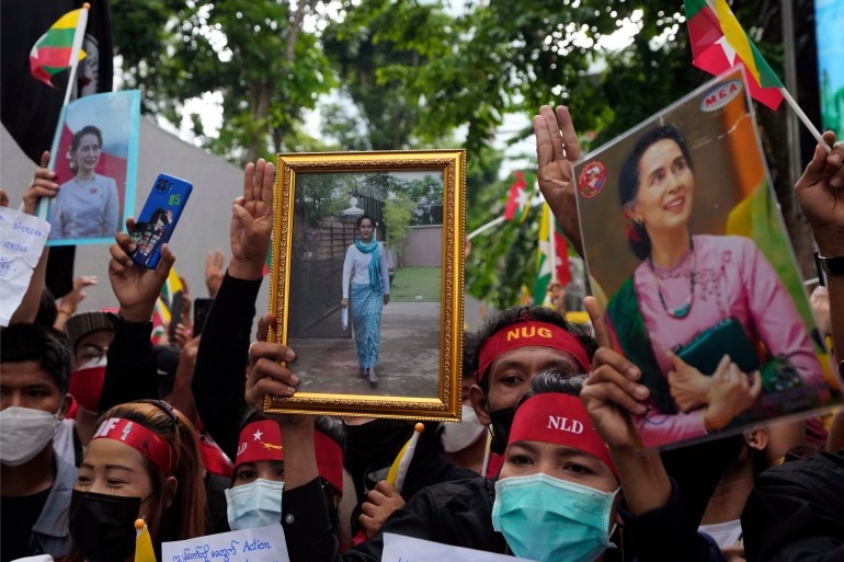 Protesters in Bangkok march with pictures of Aung San Suu Kyi. They are wearing red bandanas with NLD written in white. Some are making the three fingered salute