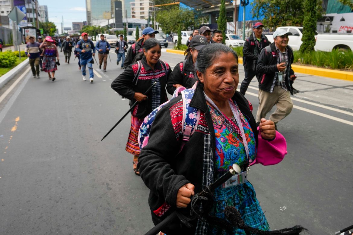 An Indigenous woman in colorful regalia marches down the streets of Guatemala City.