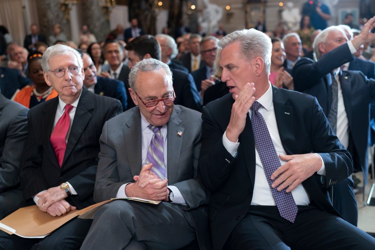 From left, Senate Minority Leader Mitch McConnell, R-Ky., Senate Majority Leader Chuck Schumer, D-N.Y., and Speaker of the House Kevin McCarthy, R-Calif., take time out from their struggle over the debt limit negotiations to attend a ceremony at the Capitol in Washington, May 17, 2023. The three men sit in a row. McCarthy holds up a hand flattened in gesture, his head turned toward Schumer. Schumer appears to be listening, his hands folded in his lap. 