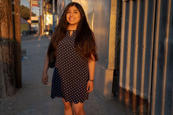 A woman in a polka-dot dress stands in the streets of Tijuana, smiling in the evening sun.