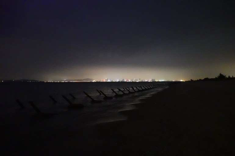 A photo of anti-landing spikes along the coast on Kinmen with the skyscrapers of Xiamen in the background at night.