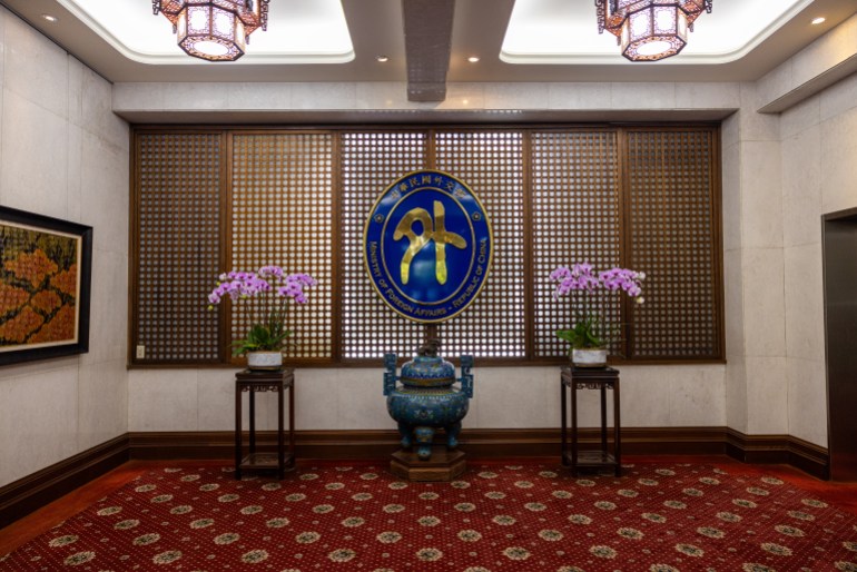 A view of the interior of the Ministry of Foreign Affairs in Taiwan. There is a screen behind with an urn in the centre and pink orchids on either side.