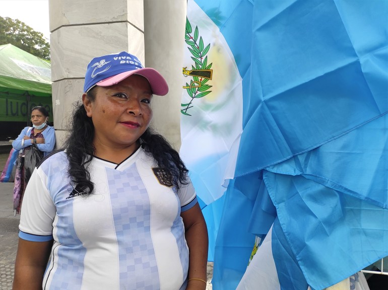 Street vendor Carmen Tino stands in front of a Guatemalan flag