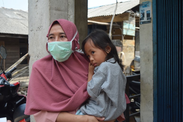 Siti, a primary school teacher in Rempang. She is wearing a pink headscarf and carrying a child. She is also wearing a face mask.