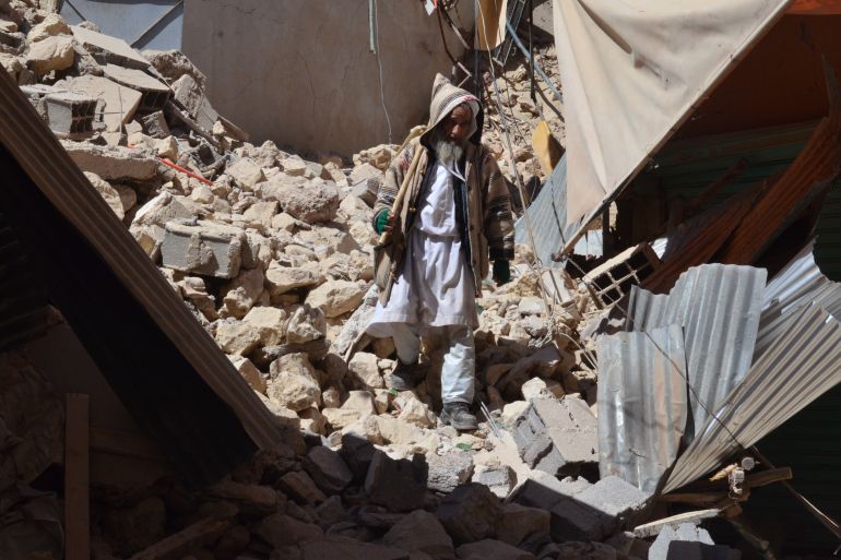 A man in a pointed hat and long white robes walks through rubble after the 2023 Morocco earthquake.