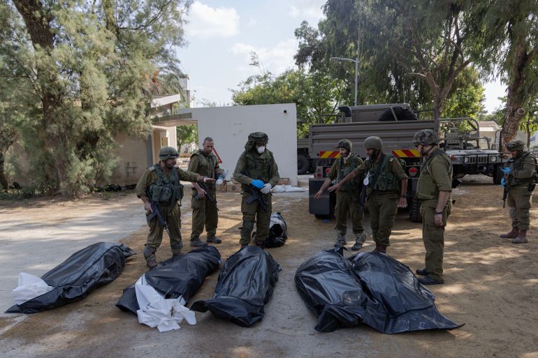 Israeli soldiers stand next to the bodies of Israelis killed by Hamas fighters in kibbutz Kfar Aza