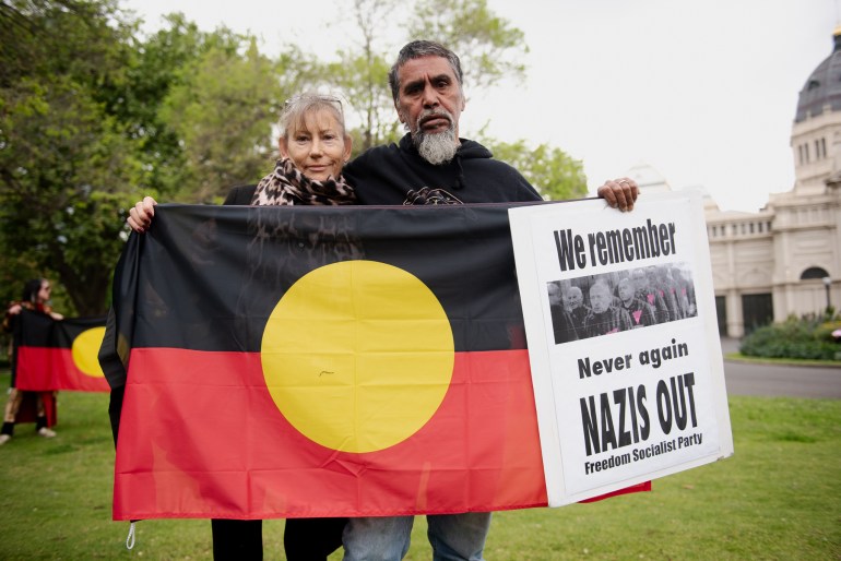 Amanda Johnstone and Ringo Terrick. They are holding an Aboriginal flag and a sign saying 'We remember, Never again, Nazis out'