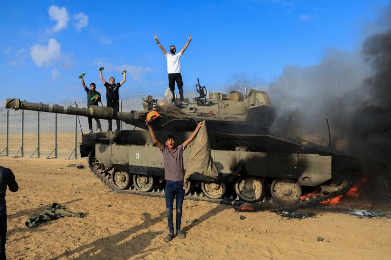 Palestinians celebrate as an Israeli military vehicle burns after it was hit by Palestinian gunmen who infiltrated areas of southern Israel