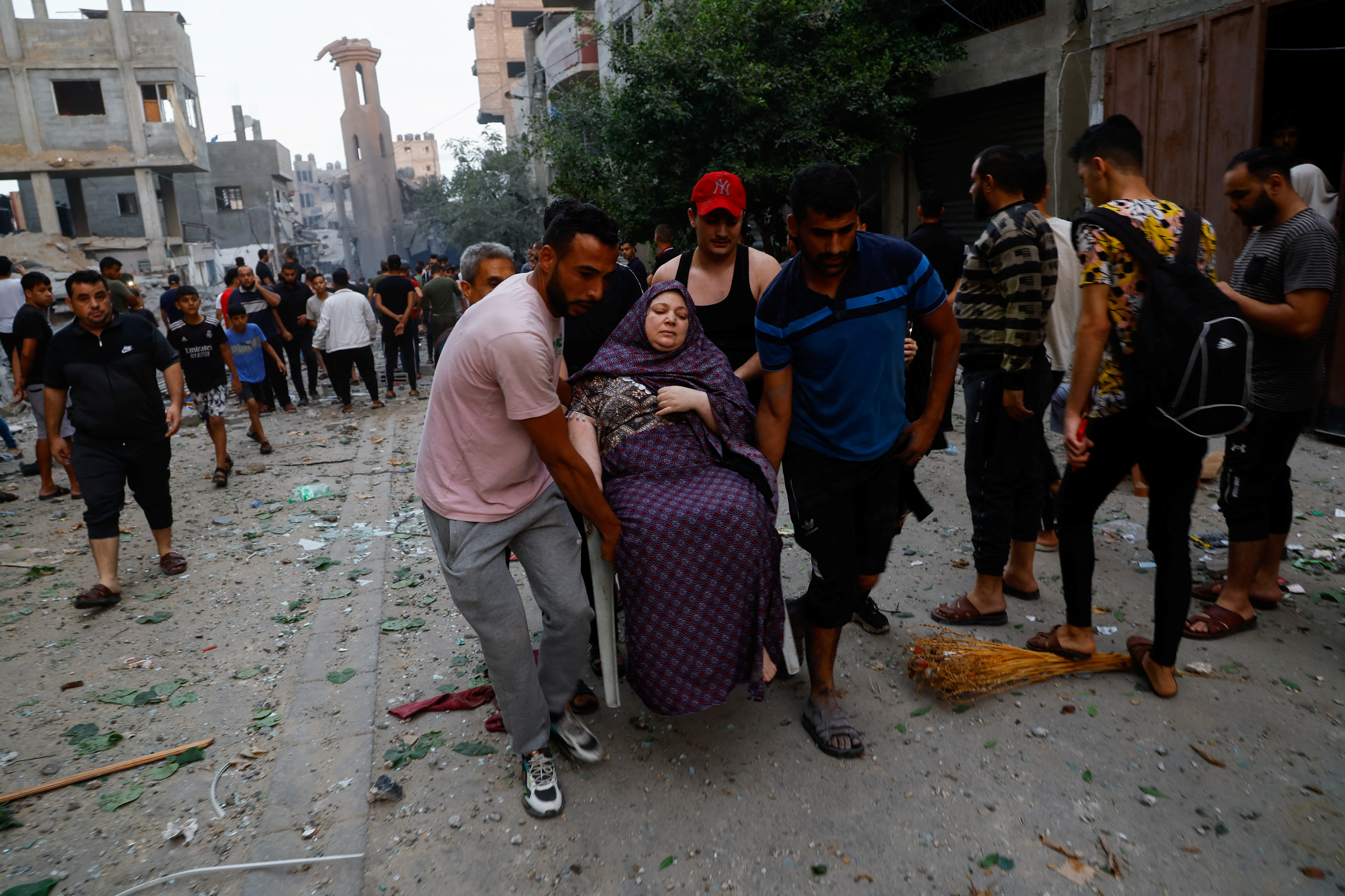Palestinians carry a woman on a debris-strewn street in the aftermath of Israeli strikes, following a Hamas surprise attack, at Beach refugee camp, in Gaza City