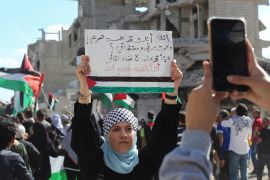 A woman shows a placard as Syrians gather during a pro-Palestinian protest to express solidarity with Palestinians in Gaza, in Yarmouk Palestinian refugee camp, near Damascus, Syria