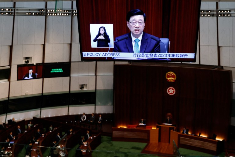 Hong Kong chief executive John Lee delivering his speech in the Legislative Council. He is seen on a large screen on the wall.