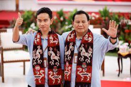 Prabowo and Gibran ahead of the registration of their candidacy They are wearing blue shirts and have scarves around their necks. They are waving.