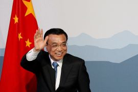 Li Keqiang waving as he walks past a Chinese flag. He is smiling broadly.