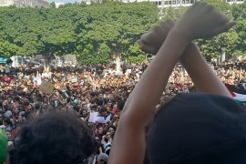 Protesters in Tunis, Tunisia, gather in front of the French embassy. In the foreground, a young protester crosses his arms above his head.