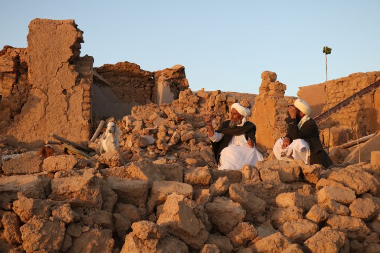 Afghan residents sit at a damaged house after earthquake in Sarbuland village of Zendeh Jan