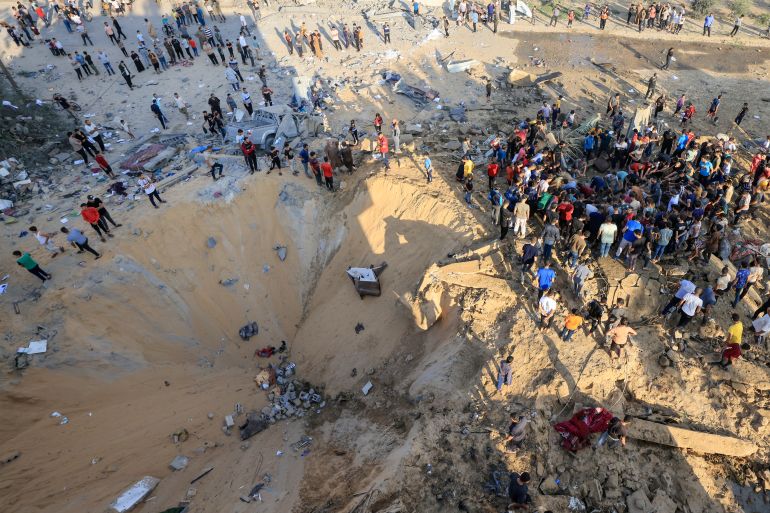 Palestinians stand next to a crater caused by an explosion from an Israeli airstrike