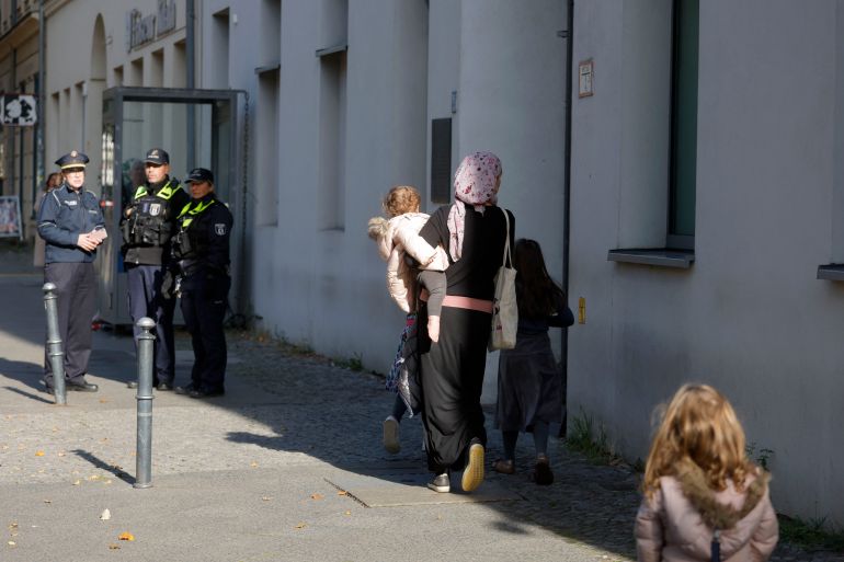 A woman walks with children as policemen stand guard in front of a building housing the synagogue of the Kahal Adass Jisroel Jewish community in Berlin, Germany, on October 18, 2023. Police in the German capital said they had opened a probe on charges of aggravated arson after assailants hurled two Molotov cocktails at the building in the Mitte district at about 3:45 am (0145 GMT). There were no reports of injuries or damage. (Photo by Odd ANDERSEN / AFP)