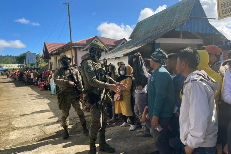 Soldiers stand guard as voters wait in line outside a polling station during the nationwide village and youth representative elections in Marawi, Mindanao island